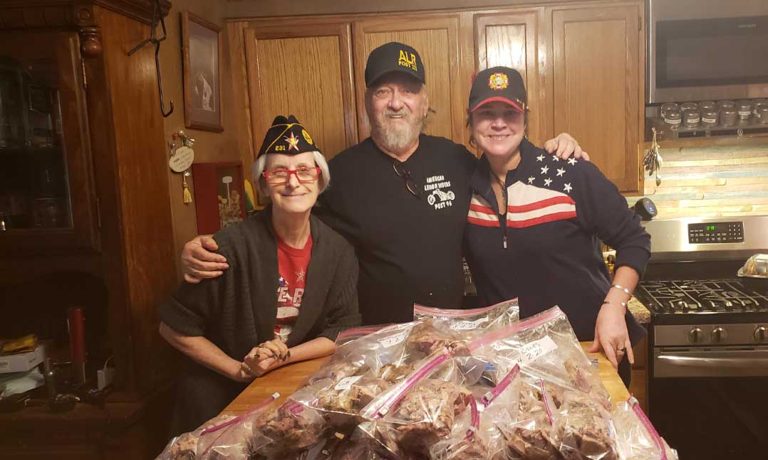 Three people stand behind a pile of smoked pork for those in need during the pandemic